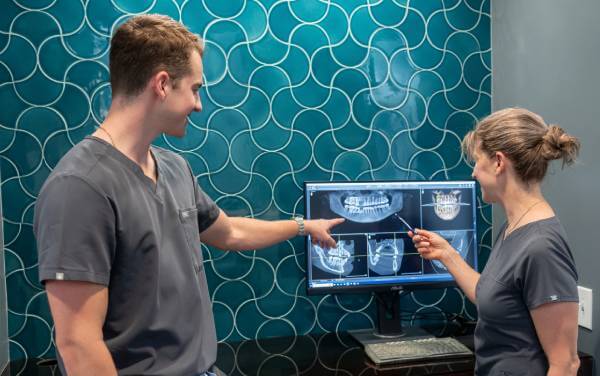 Two dental professionals discussing panoramic dental X-rays displayed on a computer monitor in a modern exam room.
