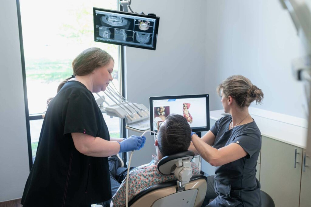 Dental team reviewing digital dental images on a computer monitor while a patient sits in a treatment chair.